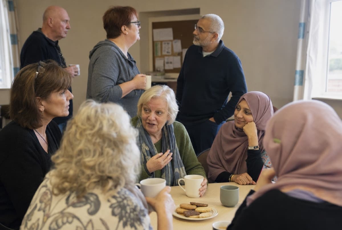 A monthly community cancer hub: adults of mixed ages talking over mugs of tea around a table in a Leicestershire community centre